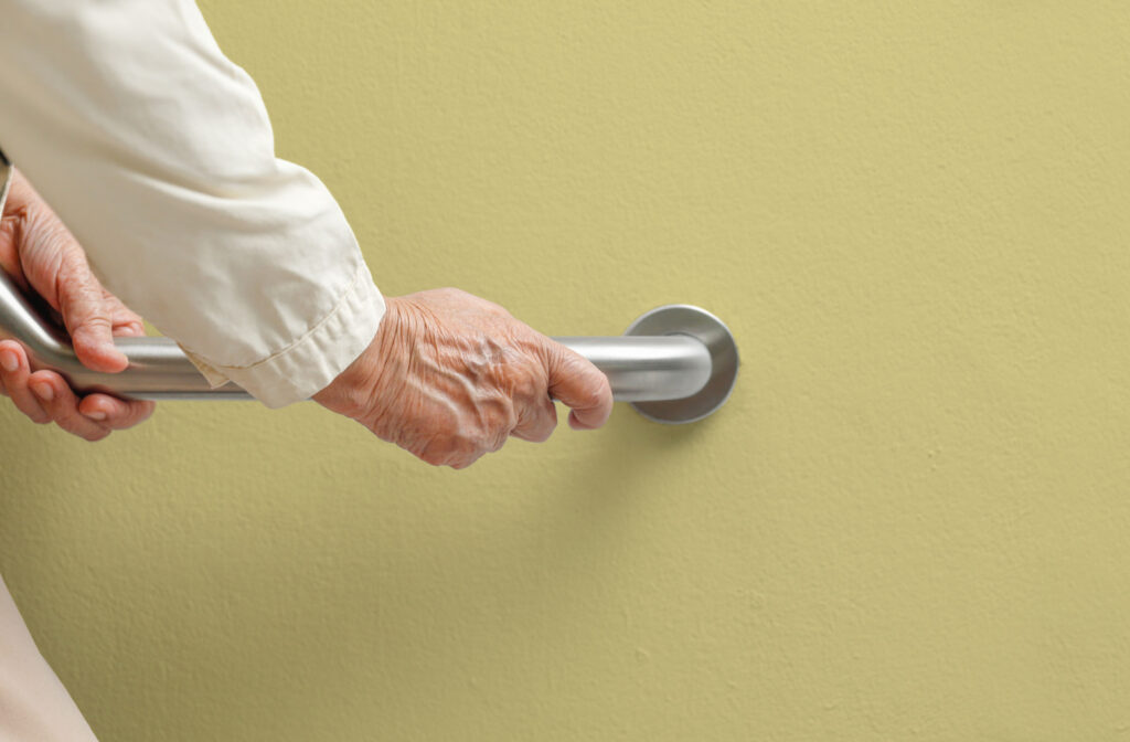 A senior person holding a railing attached to the wall to support themselves while walking down the stairs.