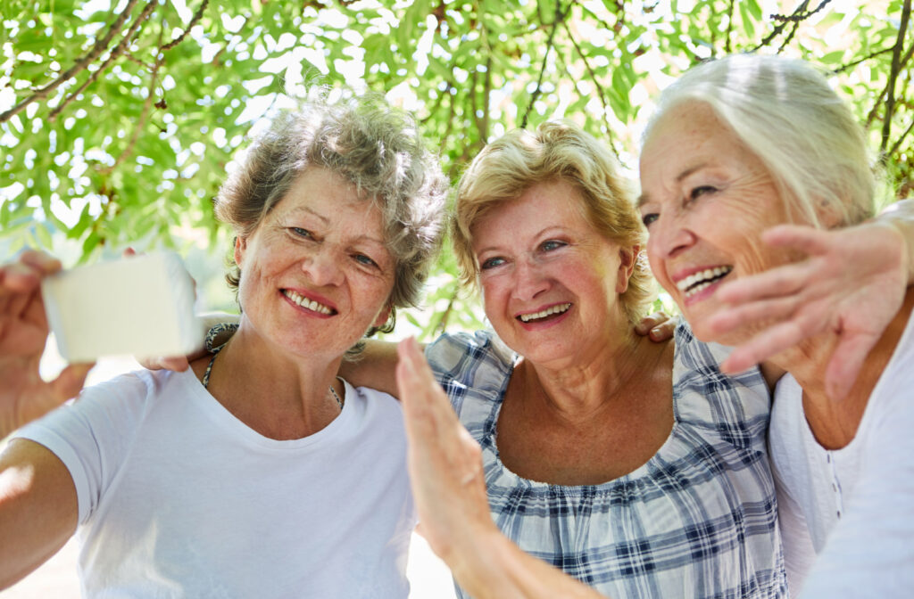 3 senior women smiling and embracing shoulders while taking a selfie outside