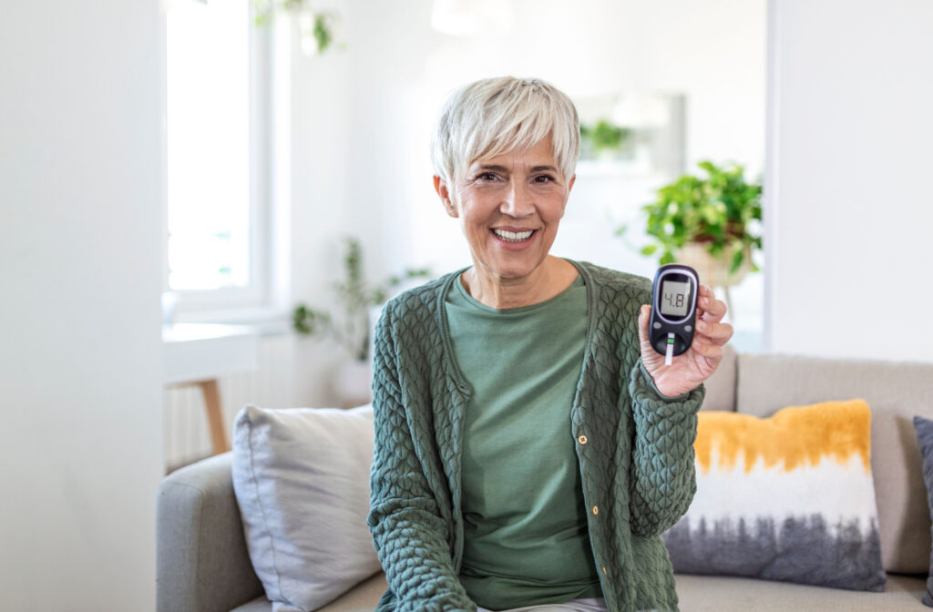 An older lady smiling and checking her blood sugar level using a glucometer and test stripe at home