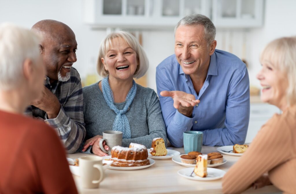 A group of older adults sitting around a table, eating and enjoying afternoon tea while smiling and chatting with each other