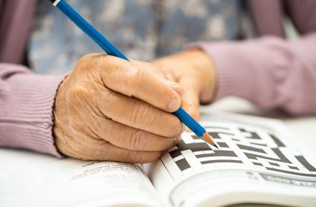 A close-up of an older adult's hands who is solving a crossword puzzle.