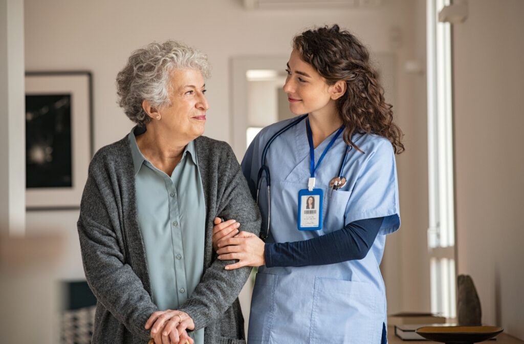 A senior woman and her caregiver in memory care linking arms and smiling at each other.