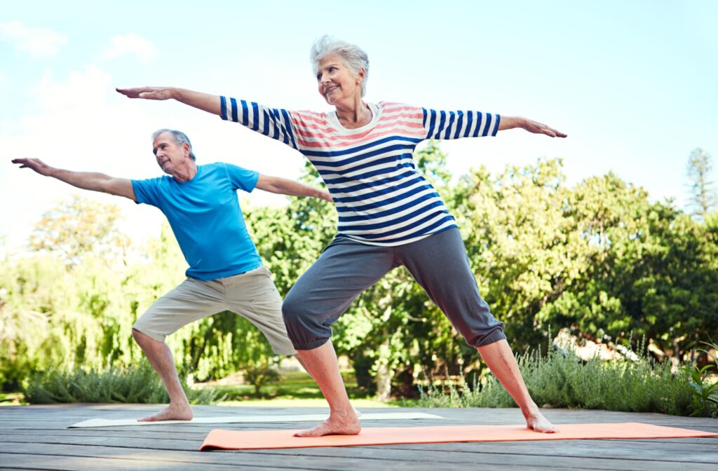 Two smiling seniors practicing yoga together outside.